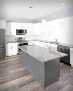 Rear of island CNC Luxor cabinets in Smokey Grey with CNC Luxor perimeter cabinets in White in the kitchen at Residences On Main in Bristol.